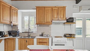 A kitchen with wooden cabinets, a microwave, a stove, and a dining table with a red tablecloth. - Apartment 'Tolis House' (Kavallouri)