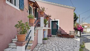 A pink building with a stone-paved entrance, a green door, and outdoor seating. - Apartment 'Tolis House' (Kavallouri)