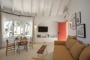 A living room with a sofa, a dining table with chairs, a TV mounted on the wall, and a red door.