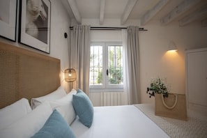 A bedroom with a bed, a window with curtains, a wall-mounted light, and a decorative bag.
