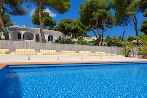 A swimming pool with lounge chairs, a wooden fence, and trees in the background.
