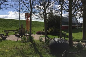 Ein Park mit einem Picknickbereich, einer roten Konstruktion und einem großen, kugelförmigen Objekt mit dem Schriftzug 'ABBA'.