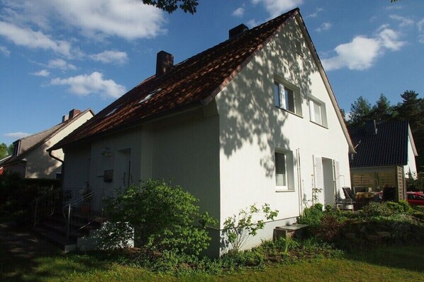 Ein zweistöckiges Haus mit geneigtem Dach, einer kleinen Veranda und einem Garten.