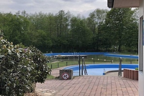 Ein Schwimmbecken mit blau-weißem Design, umgeben von einem Zaun und Bäumen im Hintergrund.