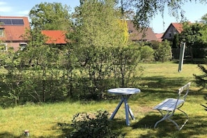 Ein grasbewachsener Außenbereich mit einem runden Tisch und einer Bank, umgeben von Bäumen und einem Zaun.