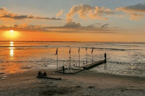 A waterfront scene with a pier, flags, and a sunset. - Holiday home with 3 bedrooms (Varel-Dangast)