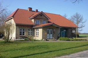 Ein zweistöckiges Haus mit rotem Ziegeldach, einer Haustür und einem kleinen Garten.