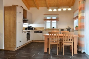 Eine Küche mit Holzausstattung, einem Esstisch mit Stühlen, einem Fenster mit Vorhängen und einem gefliesten Boden.