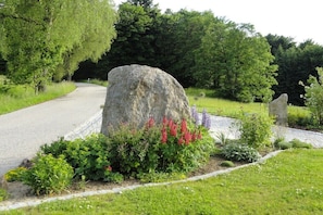 Ein angelegter Garten mit einem großen Felsen, blühenden Pflanzen und einem gepflasterten Weg.