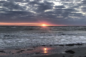 Ein Strand mit Wellen, einem Sonnenuntergang und einem bewölkten Himmel.