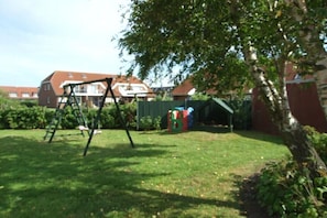 Ein Garten mit Schaukel, Spielhaus und Baum.