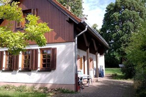 A rustic building with a white facade and wooden shutters, a covered porch, and a bicycle parked outside. - Holiday home with 2 bedrooms (Edenkoben)