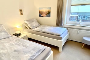 A bedroom with a bed, bedside table, lamp, and a window with a view. - Apartment in Borkum with swimming pool (Borkum)