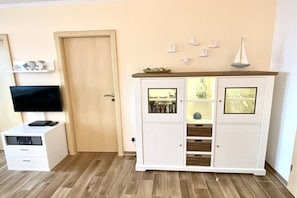 A room with a TV on a stand, a white cabinet with glass doors, and a wooden door. - Apartment in Borkum with swimming pool (Borkum)