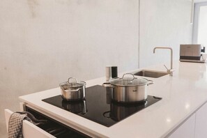 Eine moderne Küche mit eingebautem Herd, zwei Töpfen, einer Spüle und einer Kaffeemaschine.