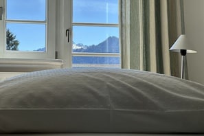 Ein Bett mit einer strukturierten Kopfstütze, ein Fenster mit Bergblick und eine Stehlampe.