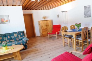 Una habitación acogedora con techo de madera, un sofá, una mesa de comedor con sillas y un armario.