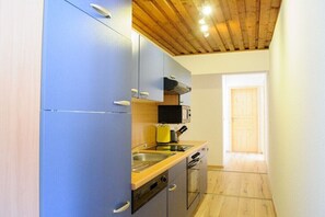 Eine kleine Küche mit blauen Schränken, einer Holzbalkendecke und einem Fenster, das natürliches Licht hereinlässt.