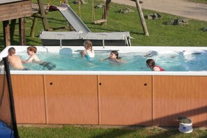 Ein Whirlpool mit vier Personen, umgeben von einer Holzterrasse und einer Rutsche.
