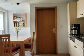 Eine kleine Küche mit Holztür, einer Kaffeemaschine und einem Bücherregal.