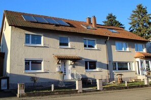 Ein zweistöckiges Wohngebäude mit Ziegeldach, mehreren Fenstern und einer kleinen Veranda.