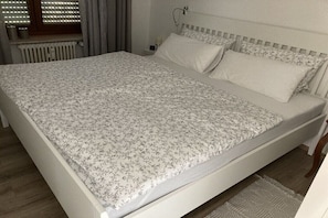 Ein Bett mit floralem Überwurf, einem weißen Kopfteil und einem Nachttisch mit Lampe.