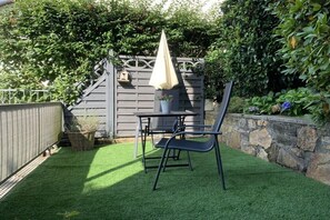 Eine Terrasse mit Tisch, Stühlen, einem kleinen Sonnenschirm und einem Blumentopf.