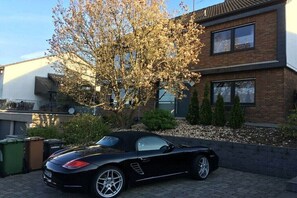 Ein schwarzer Cabriofahrwagen parkt vor einem modernen, zweistöckigen Haus mit Ziegelverkleidung und großen Fenstern.