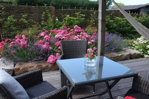 A glass-top table with wicker chairs, surrounded by a garden with various flowers. - Holiday apartment with 1 bedroom (Langballig)