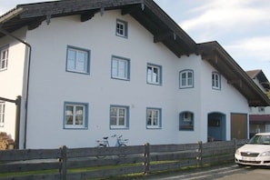 Ein weißes Gebäude mit zahlreichen Fenstern, einem Holzzaun und einem parkenden Auto.