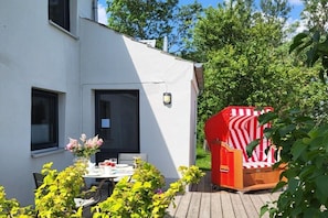 Ein weißes Gebäude mit einer Terrasse, einem Tisch mit Stühlen und einem rot-weiß gestreiften Stuhl.