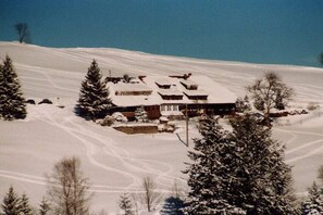 A snow-covered mountain house with a ski slope in the background. - House "Bergwiese" Ingeborg Wetzel (Todtnau)