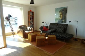 Ein Wohnzimmer mit einer Couch, Sesseln, einem Bücherregal, einem Teleskop und einem Poster an der Wand.
