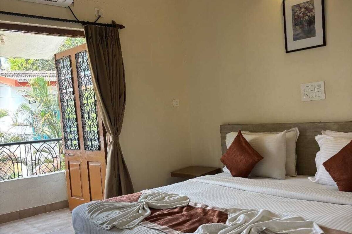 A hotel room with a bed, a window with curtains, a wall-mounted lamp, and a framed picture.