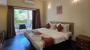 A hotel room with a bed, a ceiling fan, an air conditioning unit, a desk, a chair, and a view of the outdoors. - Lifestyle Villa (Candolim)