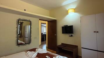 A hotel room with a bed, a ceiling fan, a mirror, a television, and a wardrobe.