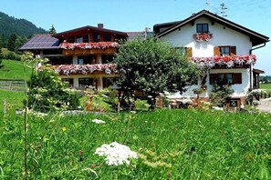 Ein zweistöckiges Haus mit Balkon, umgeben von üppiger, grüner Landschaft.