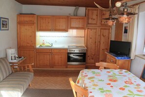 Eine kleine Küche mit Holdekor, einem eingebauten Backofen, einem Esstisch mit Blumenmuster und einem Fernseher auf einem Holzständer.