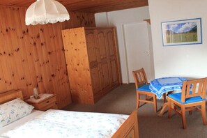 Ein Schlafzimmer mit Bett, Holzschrank, Esstisch mit Stühlen und einem an der Wand hängenden Bild.