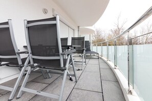 Ein Balkon mit Sitzgelegenheit im Freien, einschließlich Stühle und Tische, und einer Glasreling.