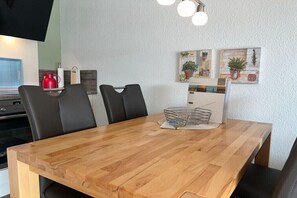 Ein Holztisch mit vier schwarzen Stühlen, einem roten Wasserkocher und einem an der Wand befestigten Fernseher.