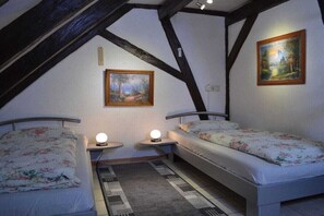 Ein Schlafzimmer mit zwei Einzelbetten, einem Nachttisch mit Lampe, einem Bild an der Wand und einer schrägen Decke.