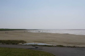 Ein weiter Sandstrand, klarer Himmel, einige Personen und ein Pier in der Ferne.