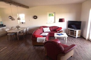 A living room with a red sofa, a television, a dining table, and a kitchen area. - Holiday apartment with 2 bedrooms (Hasselberg)