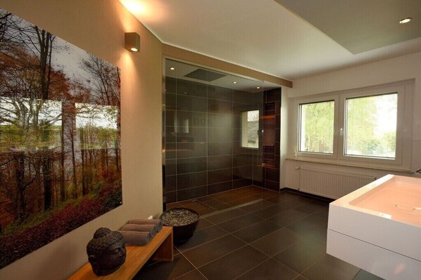 A modern bathroom with a large window, a bathtub, and a wall-mounted artwork. - ART OF LIFE the exclusive holiday apartment (Uppershausen)