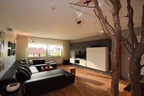 A modern living room with a sofa, a coffee table, a TV, and a tree sculpture. - ART OF LIFE the exclusive holiday apartment (Uppershausen)