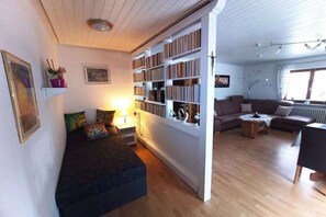 Ein Wohnzimmer mit Sofa, Couchtisch, Bücherregal und Bett.