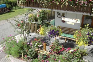 Eine hölzerne Konstruktion mit einer Bank, umgeben von einem Garten mit verschiedenen Blumen und einem Holzzaun.