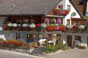 Ein mehrstöckiges Gebäude mit Balkonen, die mit Blumen geschmückt sind, einem Holzzaun und der deutlich sichtbaren Hausnummer 8 an der Fassade.