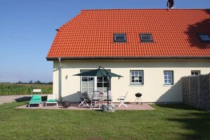 Ein Haus mit rotem Ziegeldach, einer Terrasse mit Gartenmöbeln und Blick auf ein Feld.